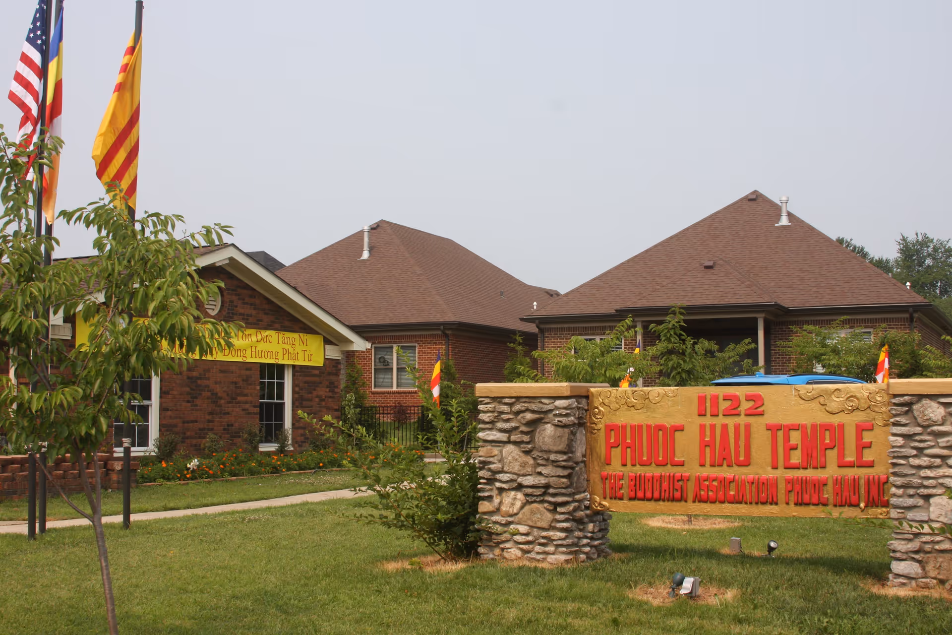 Exterior view of temple complex with brick buildings and a stone sign reading Phuoc Hau Temple.