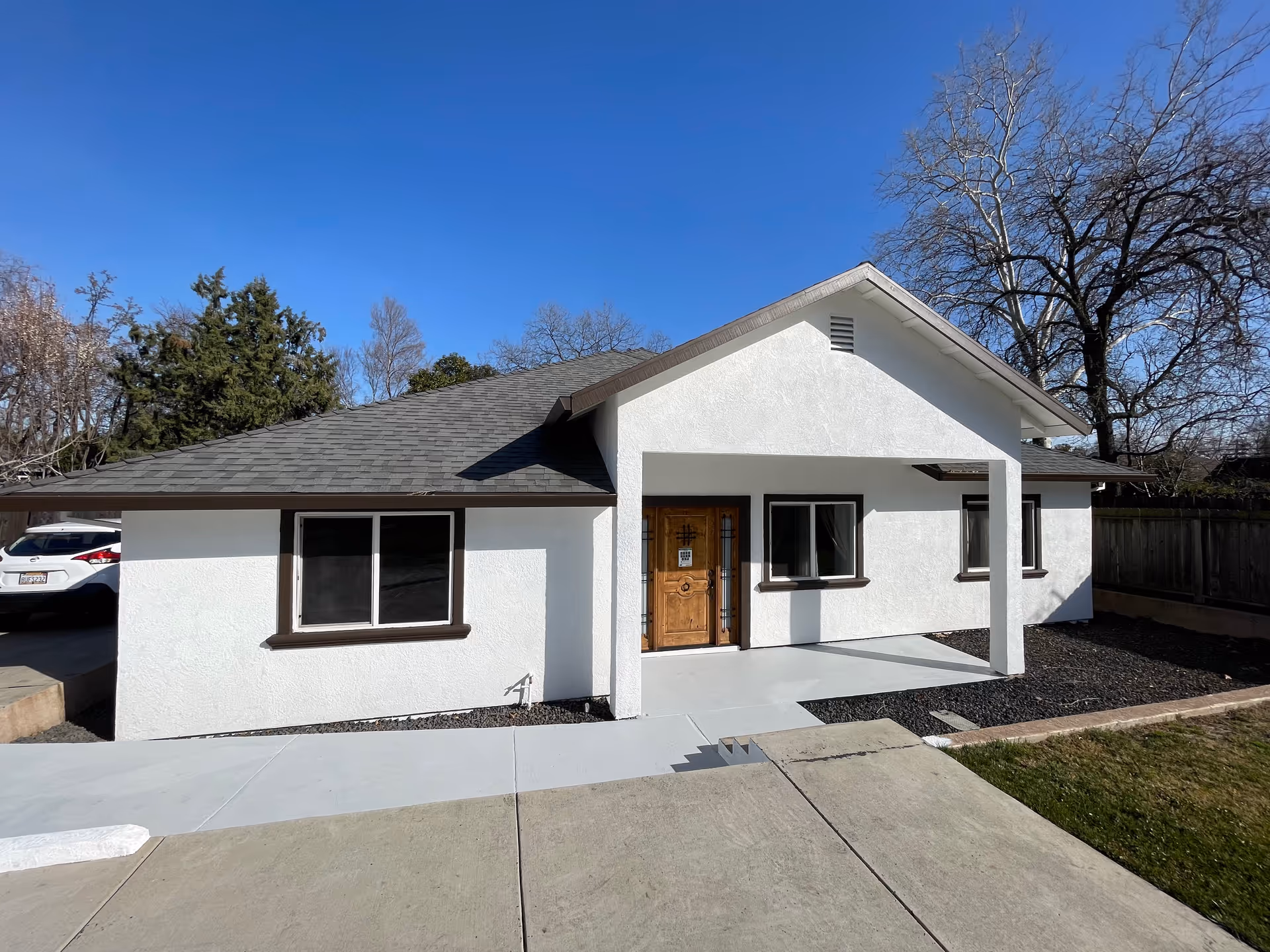 Front exterior of a single-story white building with a covered porch, wooden door, and paved walkway.