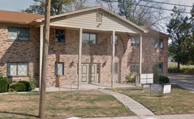 Brick two-story building with double entry doors, signs, and a walkway to the entrance.