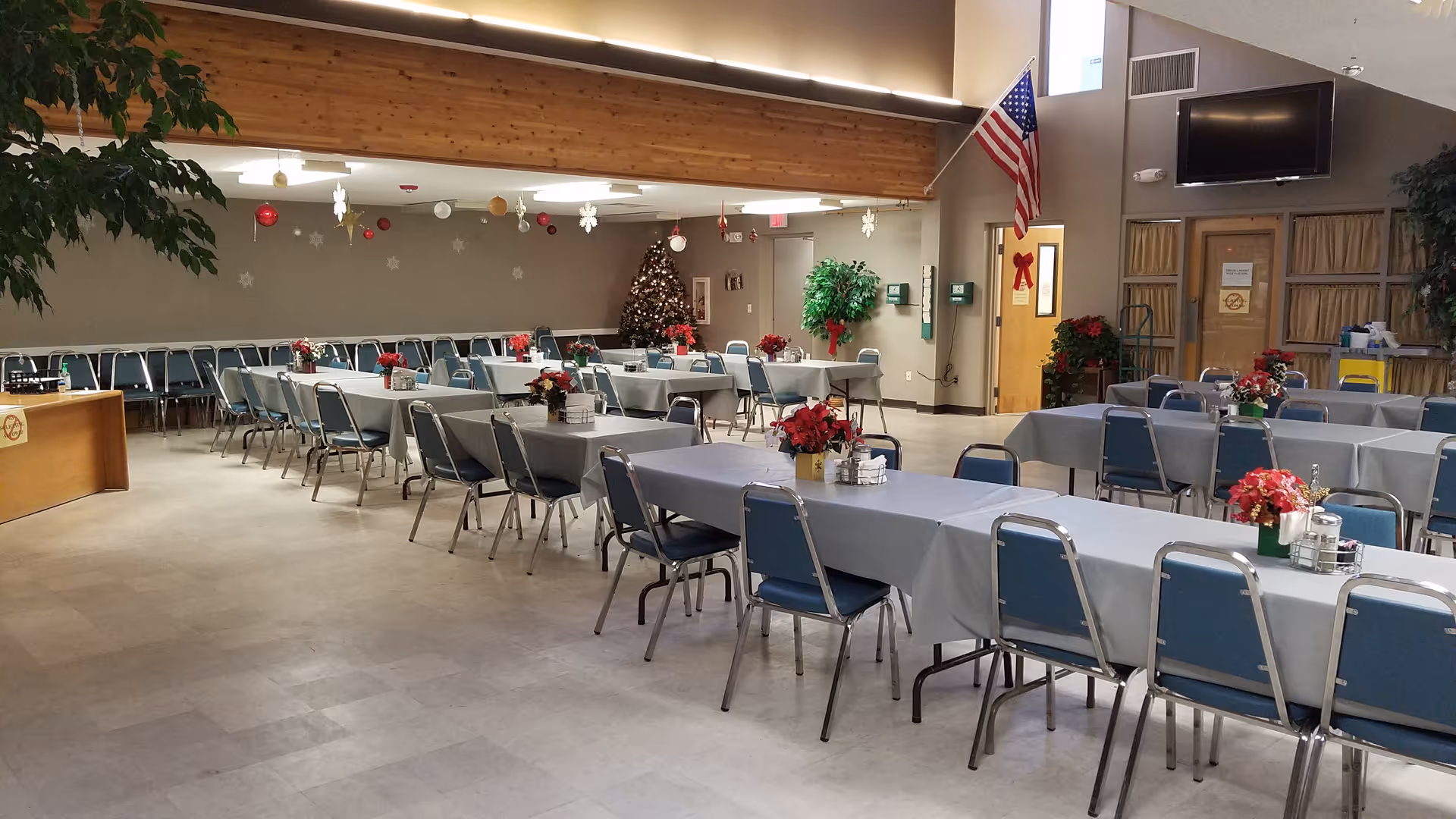 A spacious dining hall with long tables, blue chairs, and holiday decorations.
