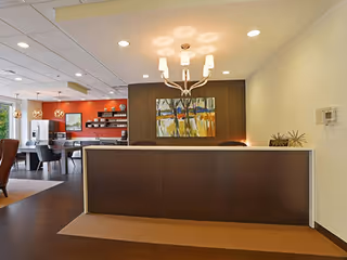 Reception desk in a senior living facility lobby with chandelier, artwork, and warm wood tones.