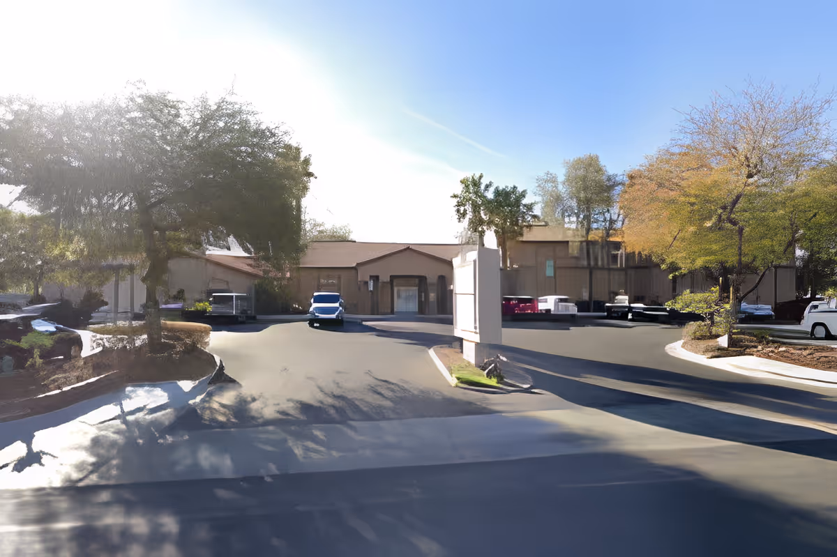 Driveway and front entrance of a low-rise assisted living building with parked cars and trees.