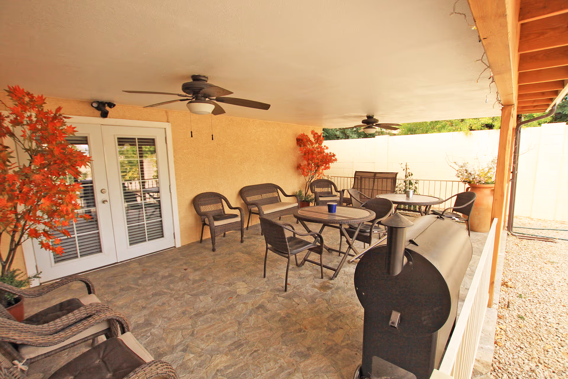 Covered outdoor patio with seating, tables, ceiling fans, a grill, and doors to the building