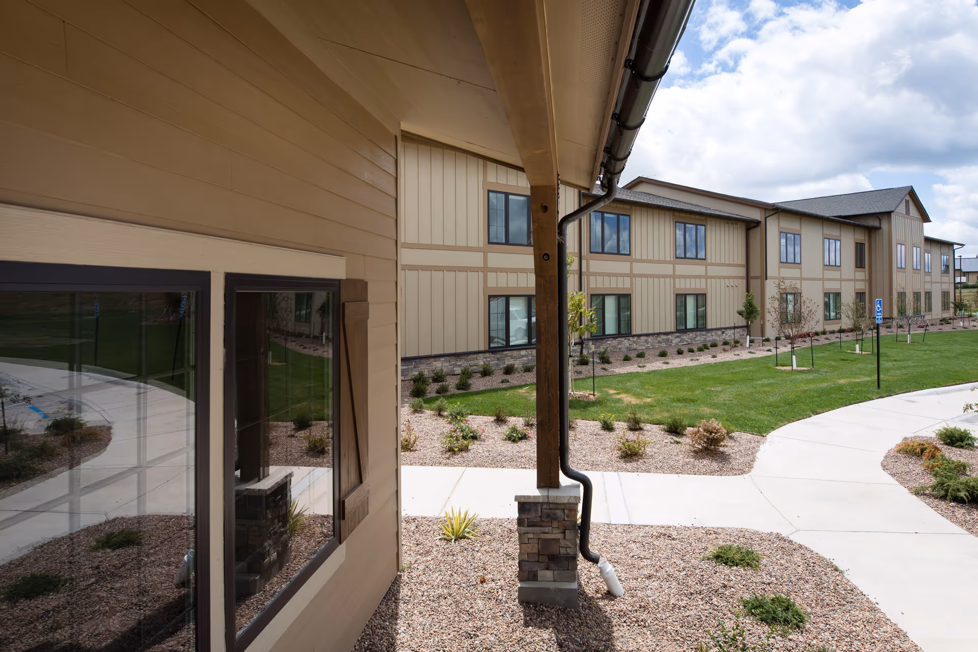 Exterior view of a two-story beige senior living building with windows, landscaped grounds, and a curved concrete walkway.