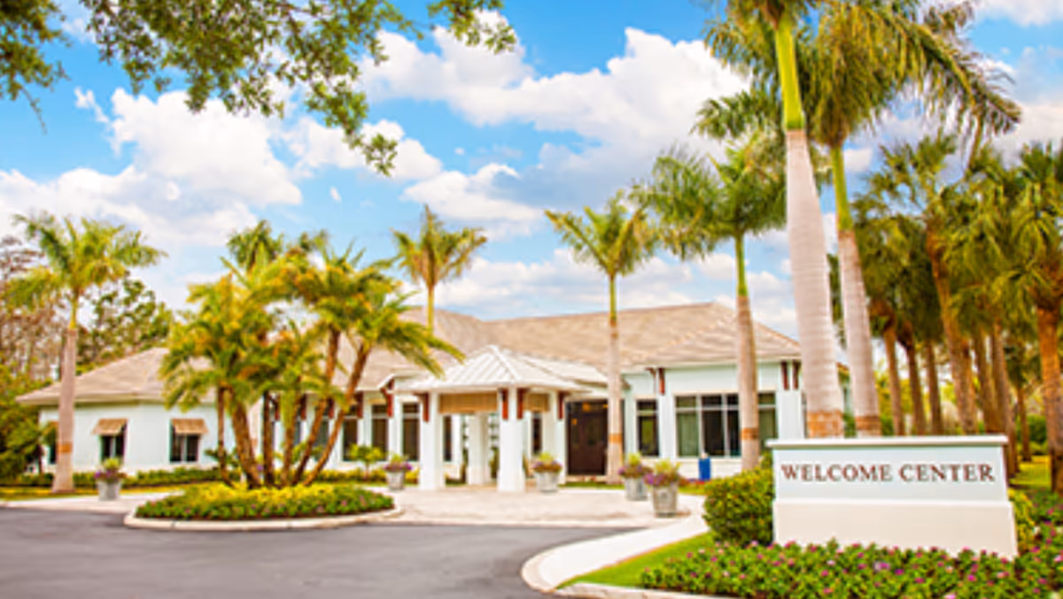Front entrance of a single-story building with a 'Welcome Center' sign, palm trees, and a landscaped circular driveway.
