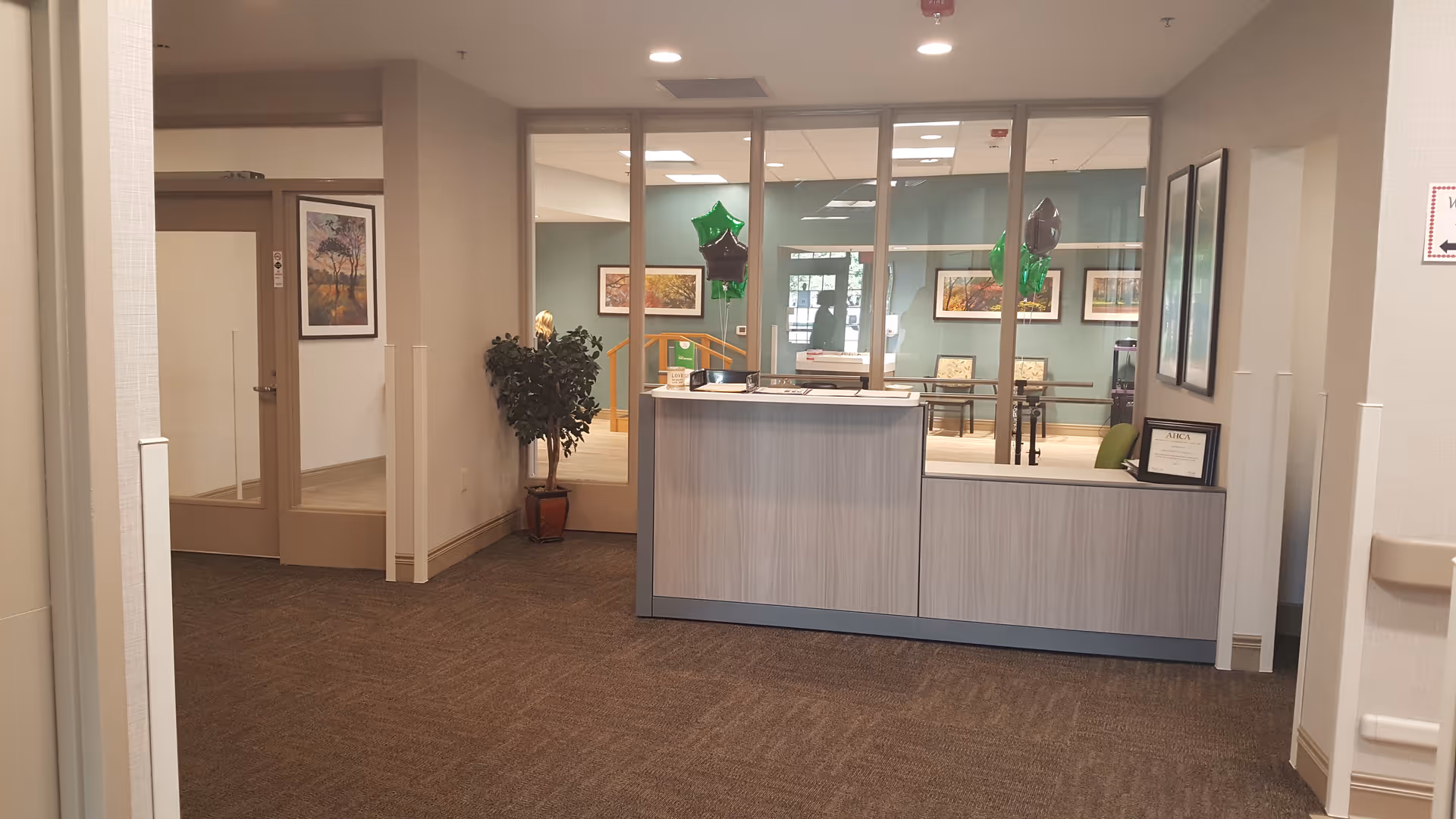 Reception desk and seating area inside a senior living facility lobby with framed art and decorative balloons.