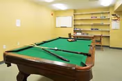 Yellow recreation room with a billiards table, cues, and wall shelves.