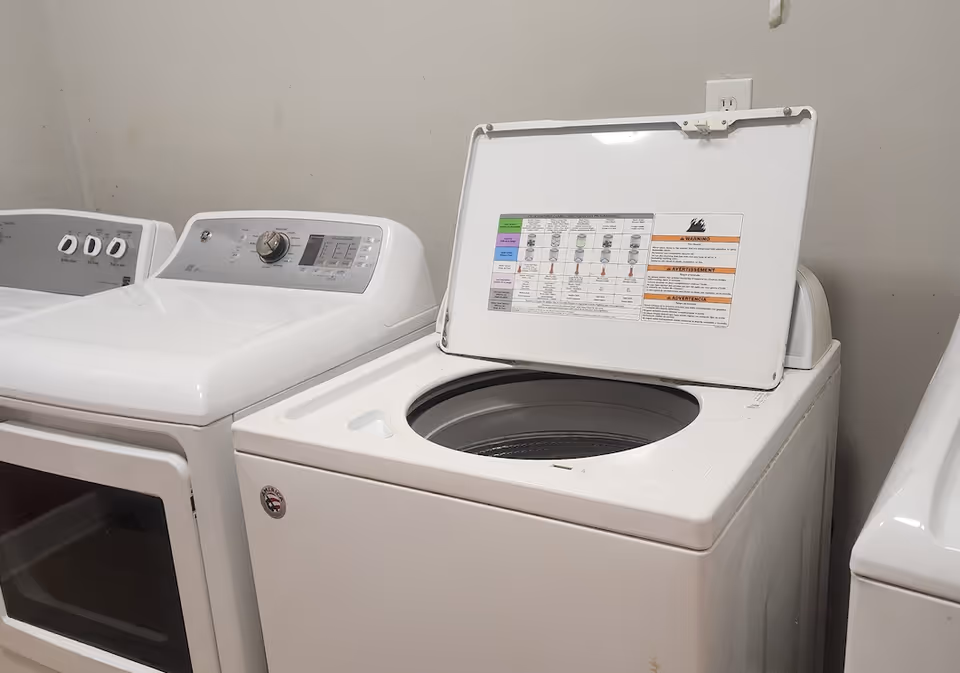 Three white top-loading machines in a small facility laundry room.