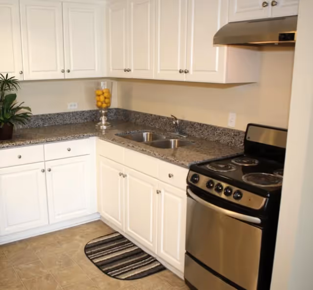 Bright kitchen with white cabinets, granite counters, sink, stove, and decorative lemon jar.
