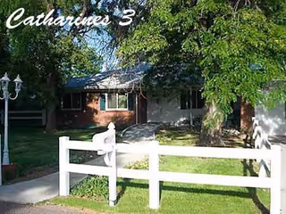 Front yard with white fence and brick house, shaded by trees.
