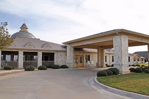 Stone-clad senior living facility entrance with a covered porte-cochere and manicured landscaping.
