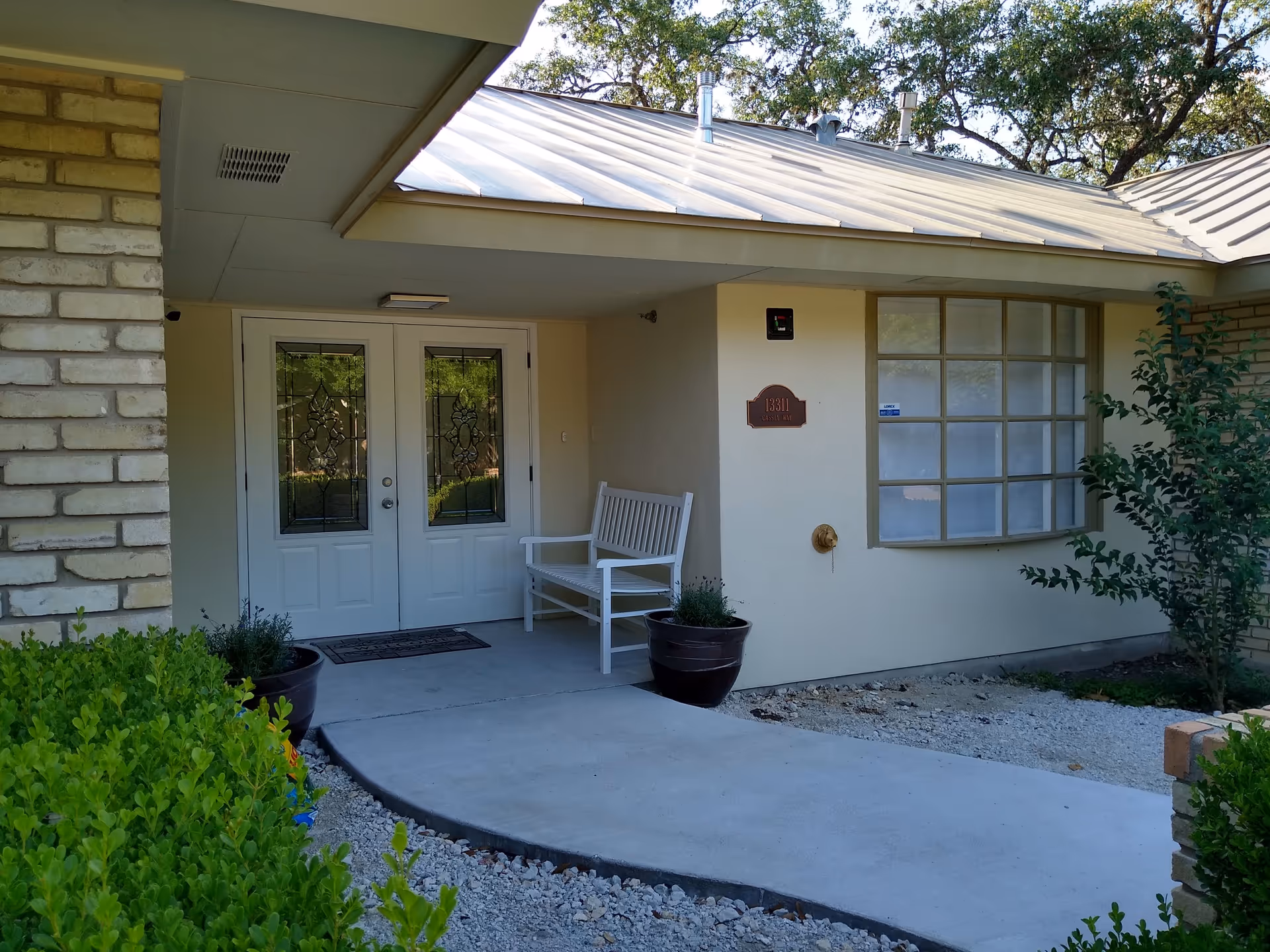 Front entrance of Red Oak Memory Care building with double doors, bench, and potted plants.