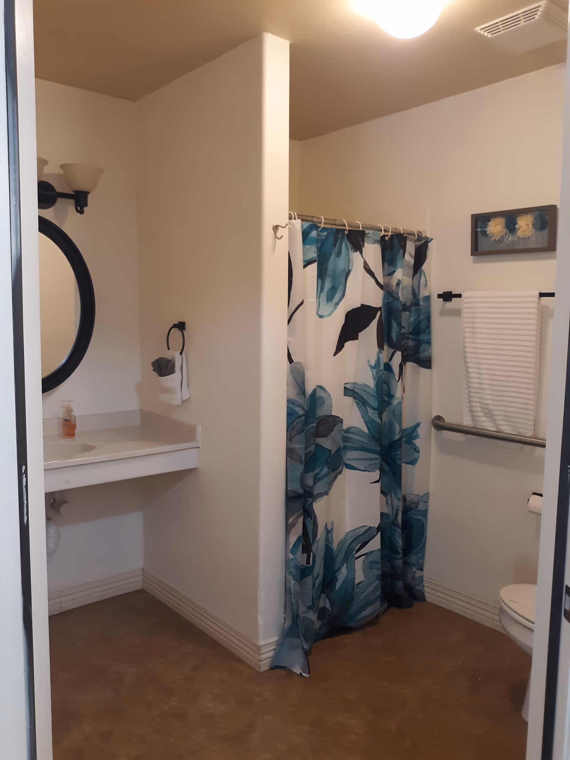 Small bathroom with sink, mirror, shower curtain, towel rack, and visible toilet.