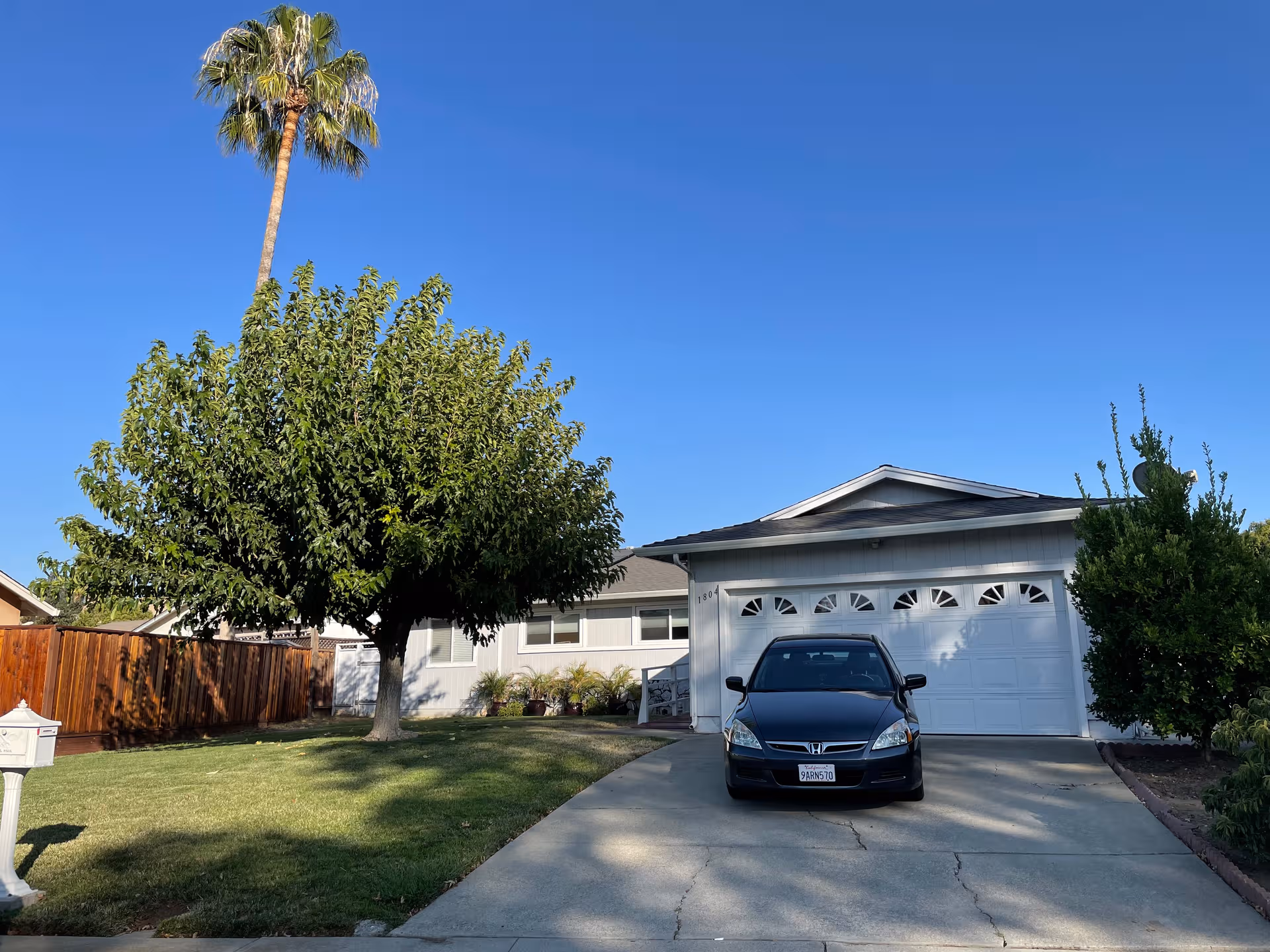 A single-story house with a driveway, car, trees, and a clear blue sky