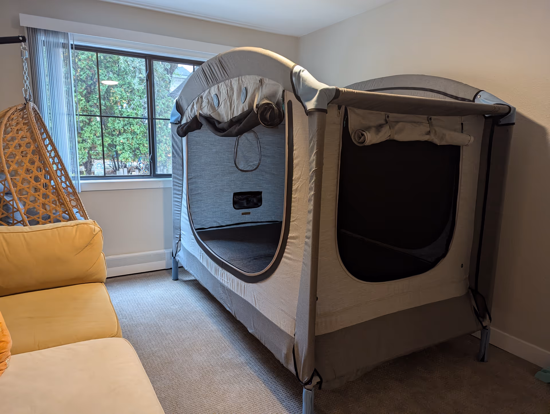 Interior living room with a large gray medical privacy tent beside a window.