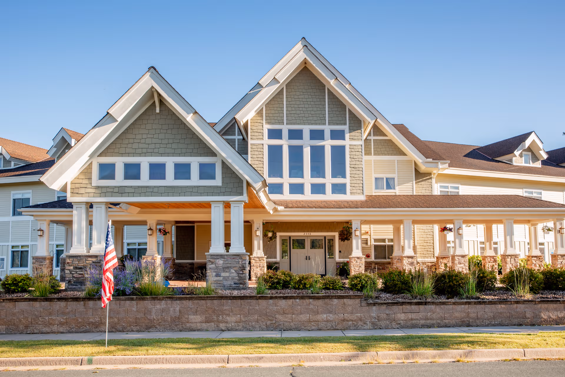 Stone and siding senior living facility with a covered porch, columns, and American flag.