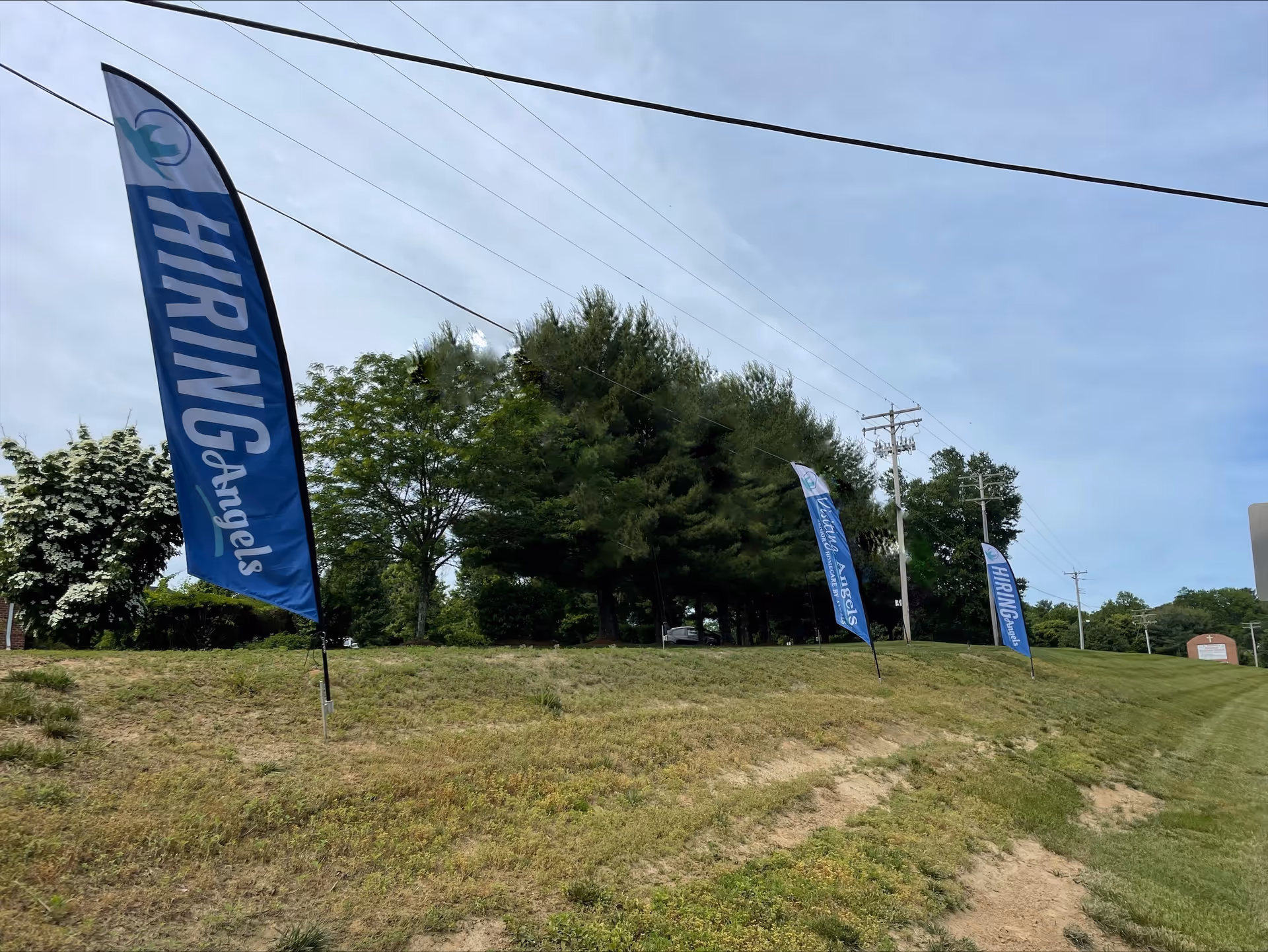 Blue banners line a grassy roadside with trees near a senior care facility.