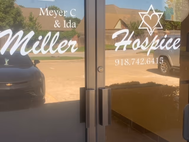 Glass doors display Miller Hospice signage with reflections of parked cars and building exterior.
