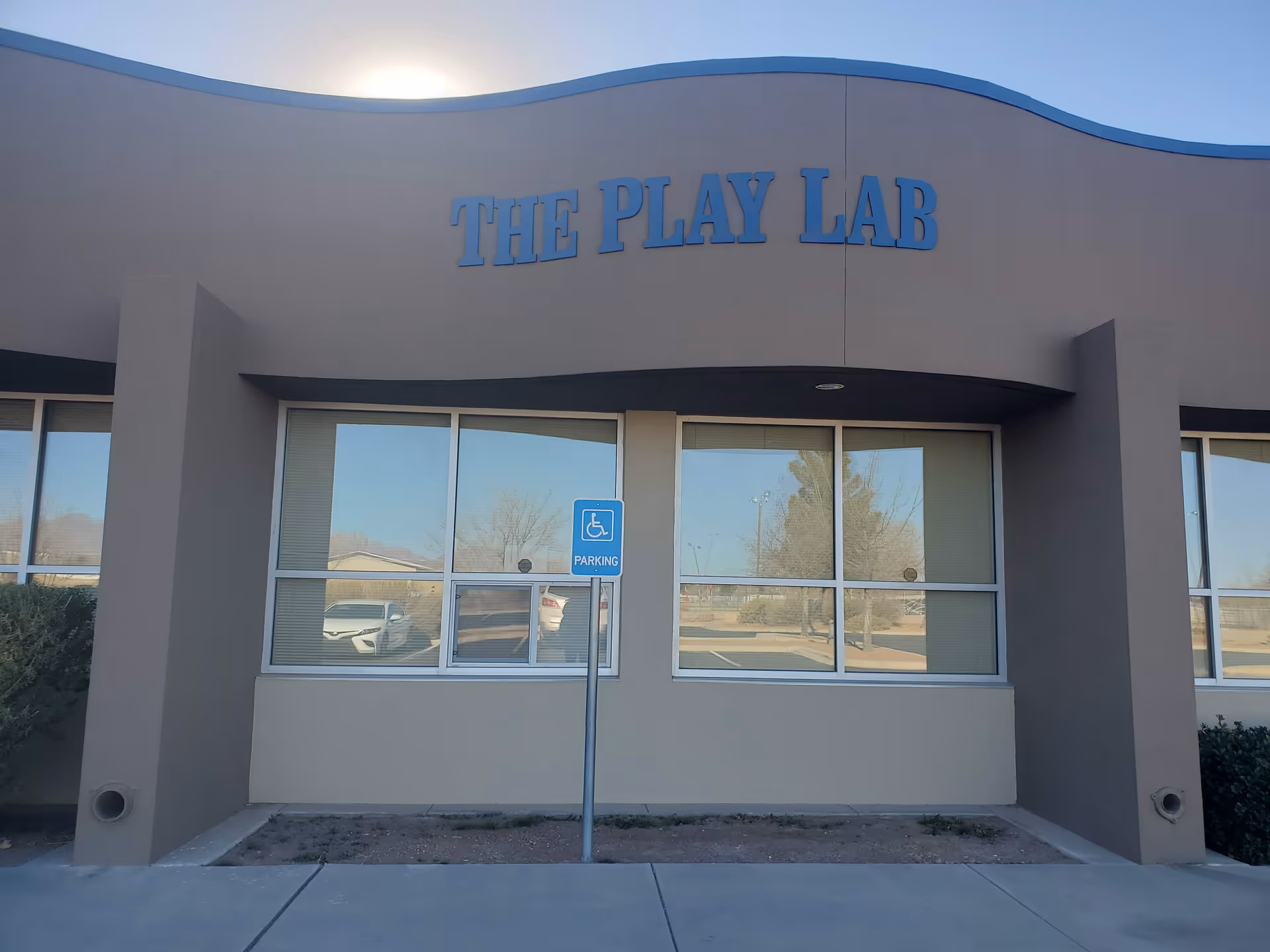 Exterior of The Play Lab facility with large windows, curved roofline, and handicapped parking sign.
