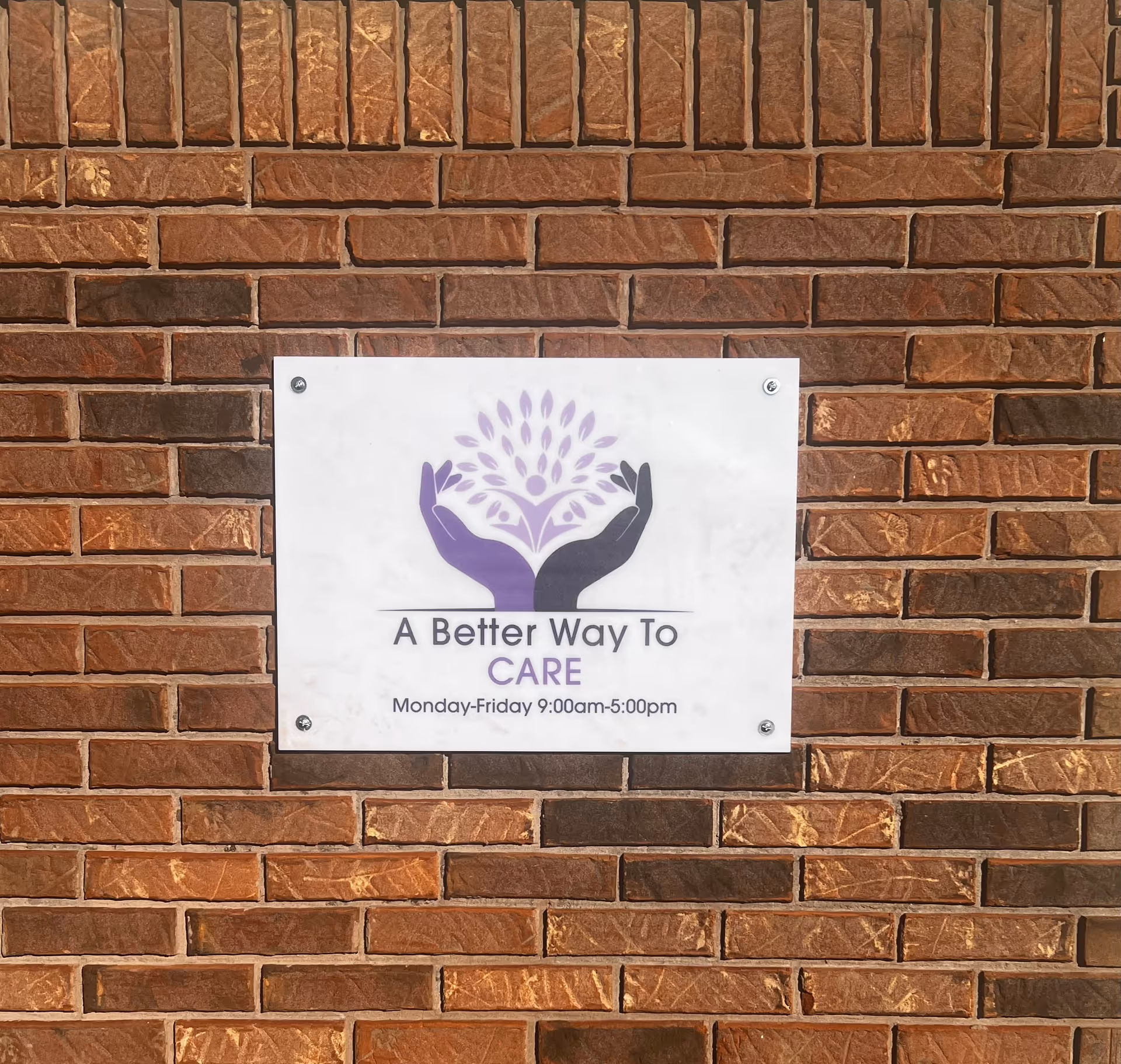 Sign on brick wall reads 'A Better Way To CARE' with purple hands logo