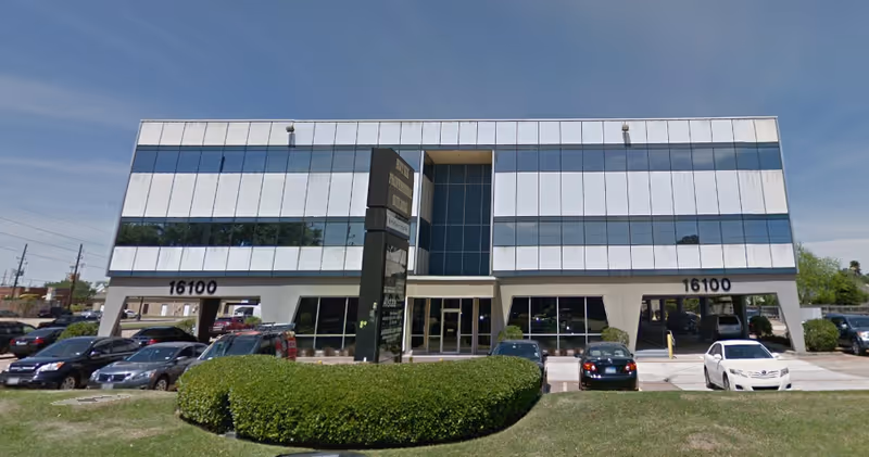 Exterior view of a modern office building with a tall black sign and several parked cars.