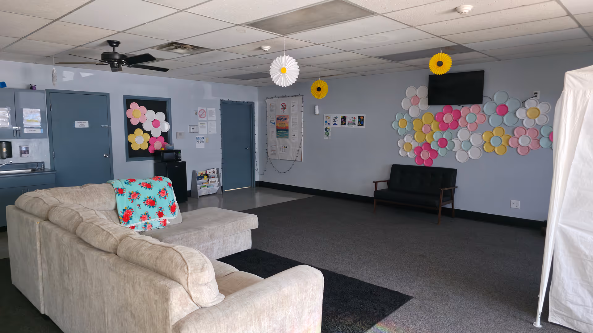 Spacious senior living lounge with a beige sofa, chairs, wall decorations, and a TV.