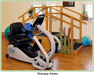 Recumbent exercise machine in a bright therapy room near a wooden staircase.