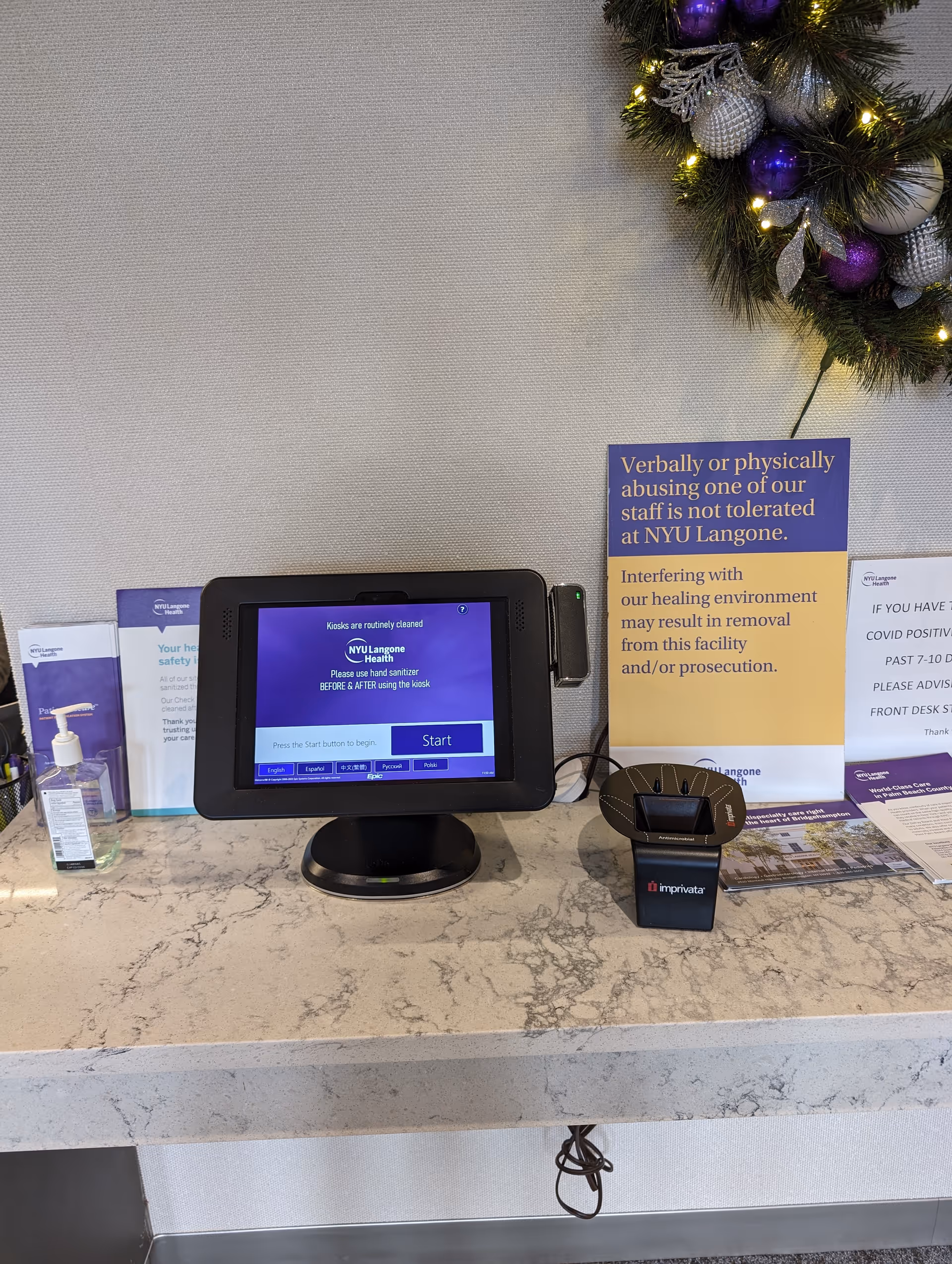 Interior reception desk with touchscreen kiosk, card reader, sanitizer, and wreath.