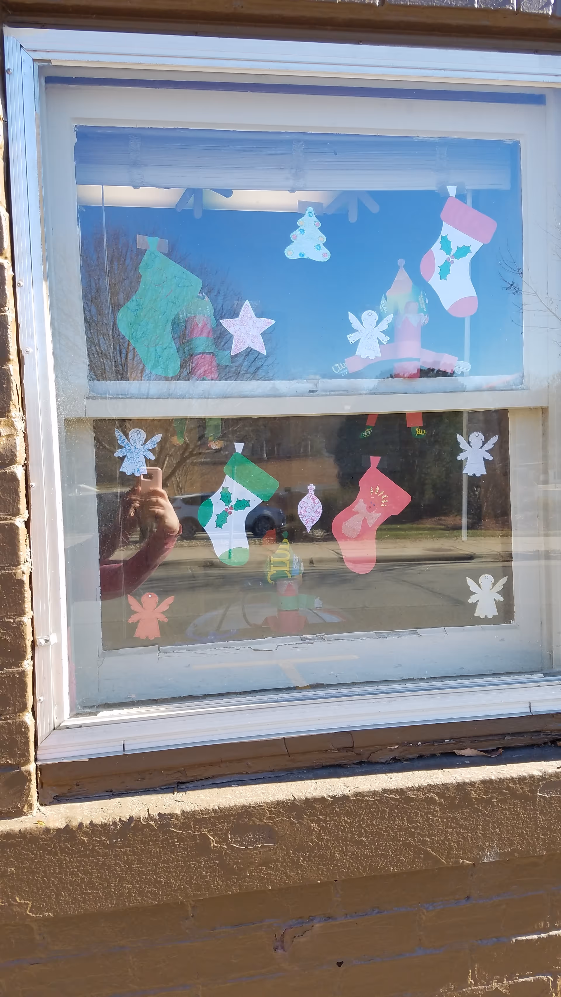 Window decorated with colorful holiday cutouts and street reflections outside.