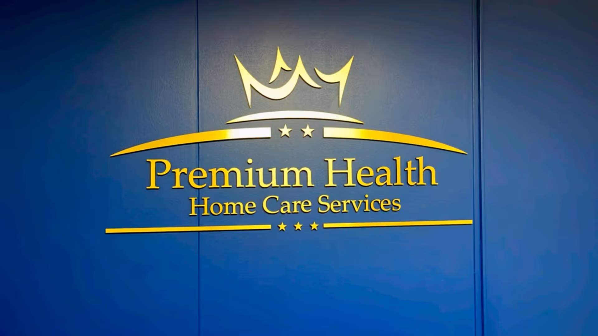 Blue wall with yellow Premium Health Home Care Services sign and crown logo