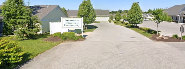 Entrance to Sycamore Retirement Community with a sign, trees, and a paved driveway.