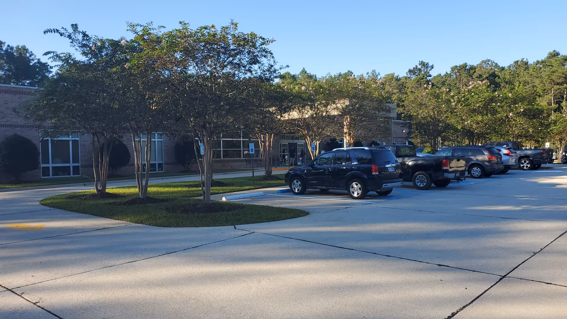 Parking lot in front of a low-rise medical building, with trees and row of parked cars.