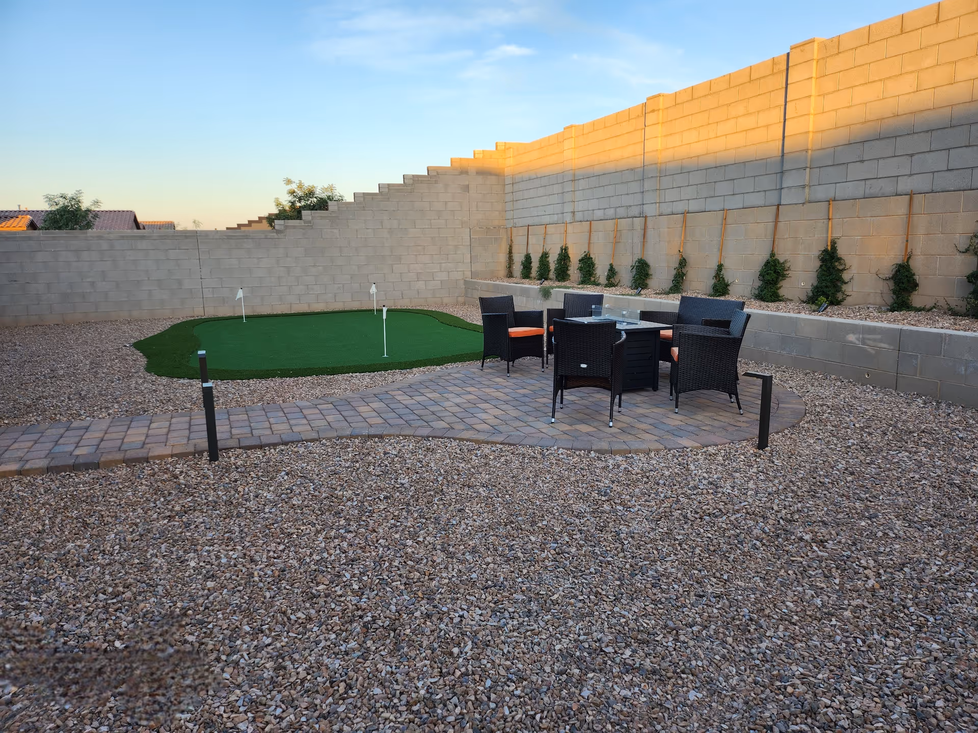 Outdoor courtyard with seating area and a small putting green by a tall block wall.