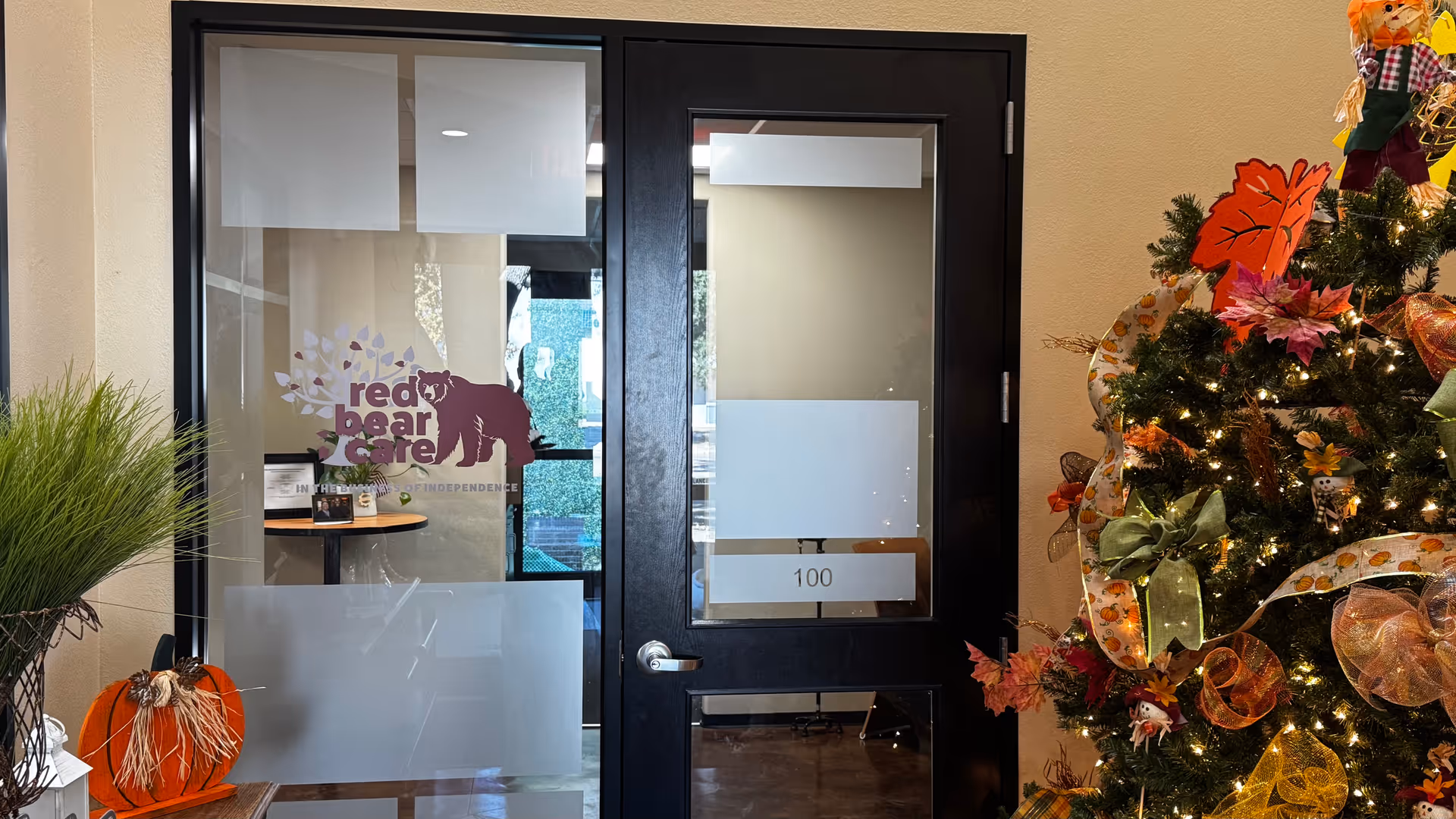 Interior hallway with glass door labeled 100, Red Bear Care logo, and a Christmas tree.