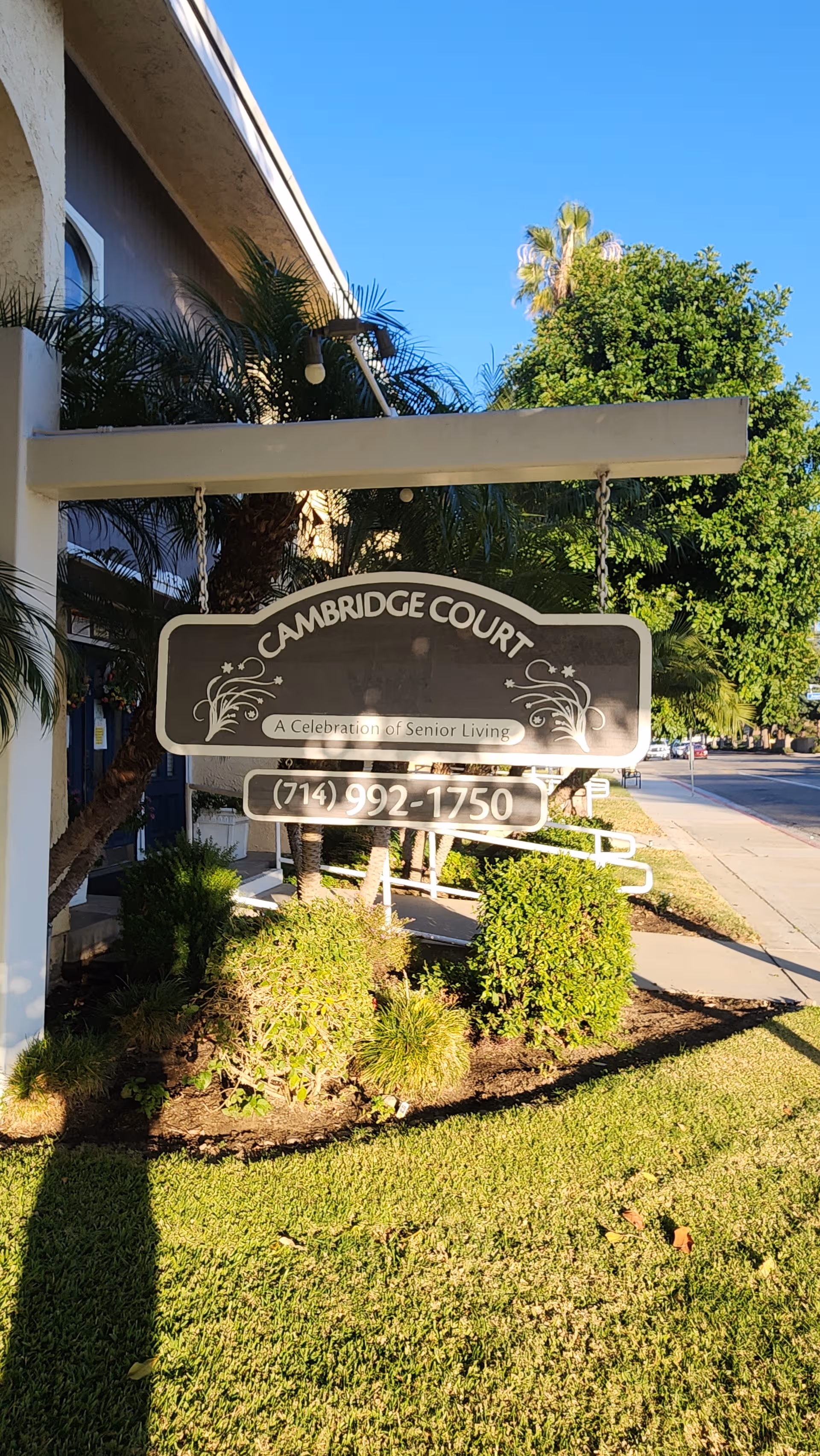 Front view of Cambridge Court Assisted Living sign near entrance with greenery and blue sky