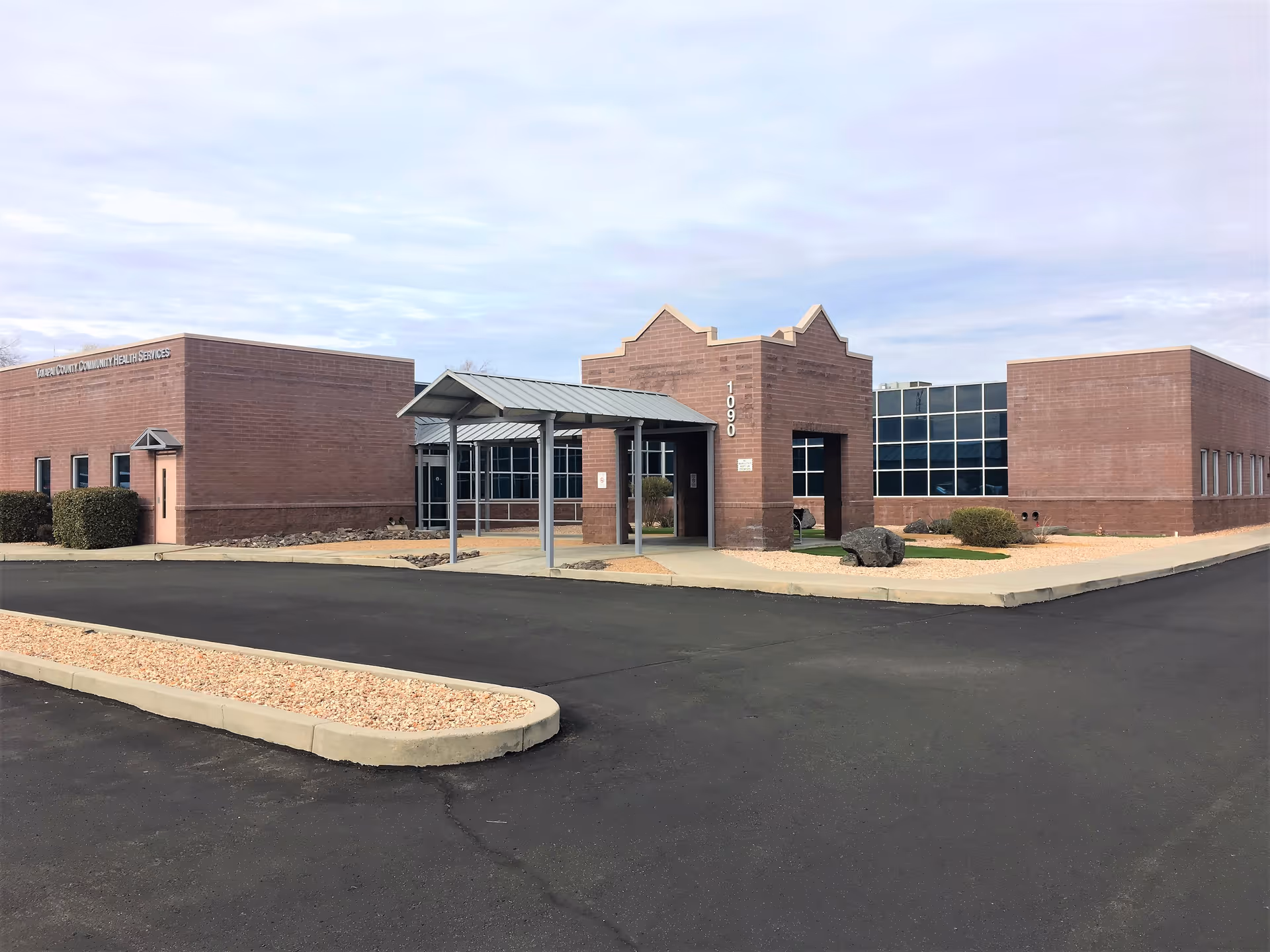 Brick building with a covered entrance, large glass windows, and surrounding parking.