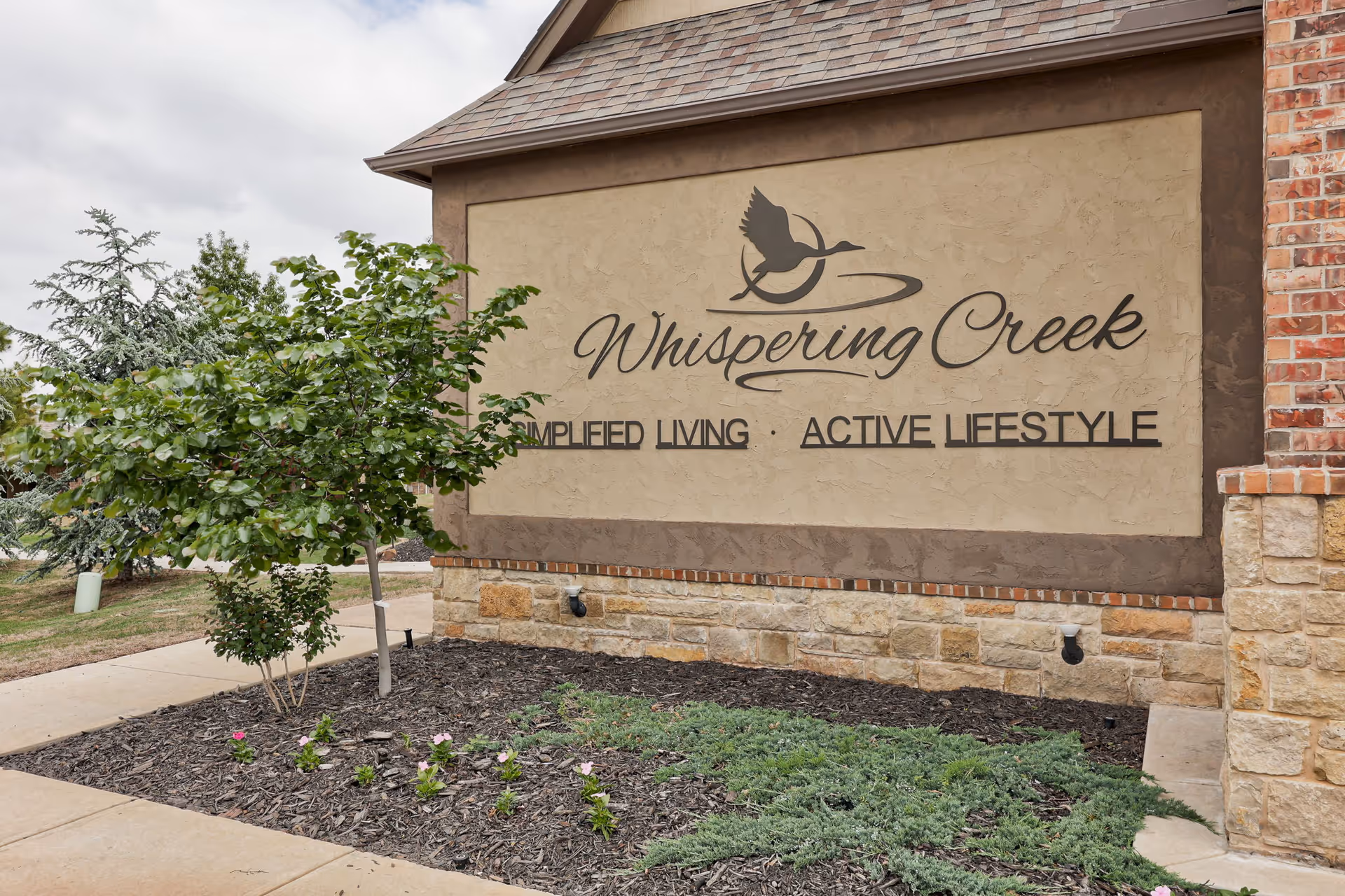 Exterior entrance sign for Whispering Creek on a stone wall with surrounding landscaping.