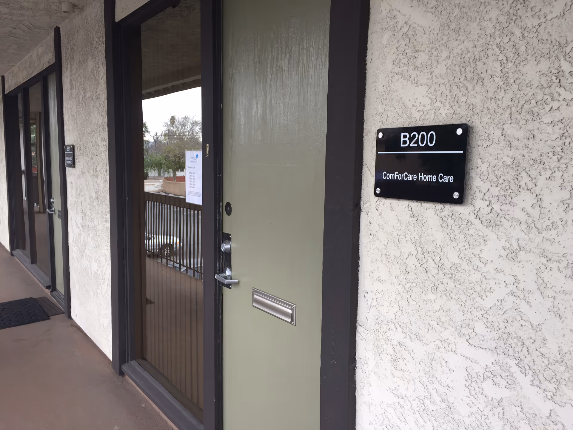 Exterior corridor entry with green door and B200 ComForCare Home Care plaque.