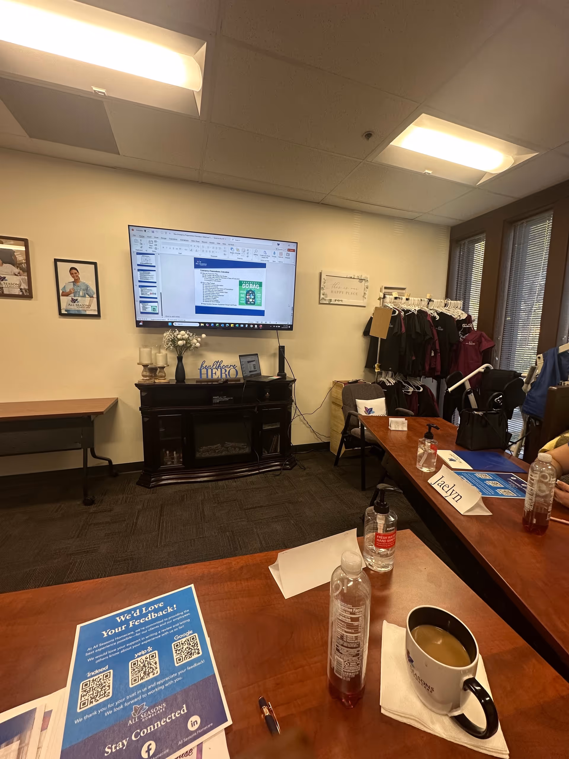 Interior conference room with a mounted TV, tables, and a coat rack in All Seasons Homecare.