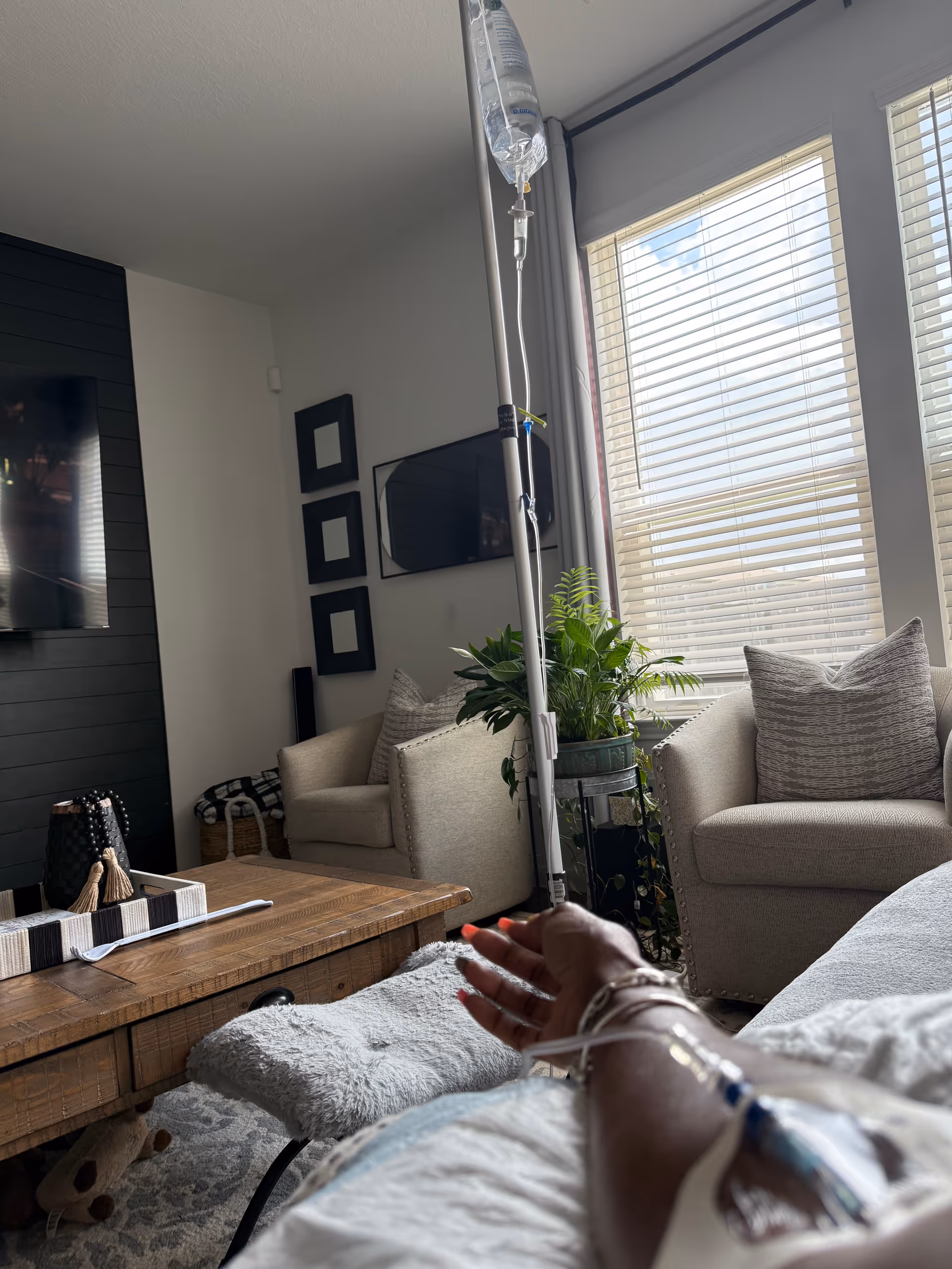 IV drip stands beside a sofa in a bright living room with a patient arm.