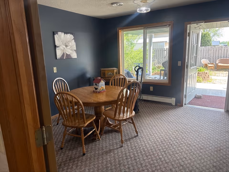 Indoor dining room with round wooden table, several chairs, blue walls, and a door to a patio.