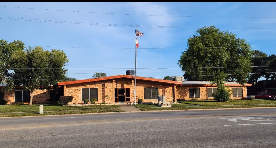 Brick single-story rehabilitation center exterior with flagpole, windows, and a manicured lawn.