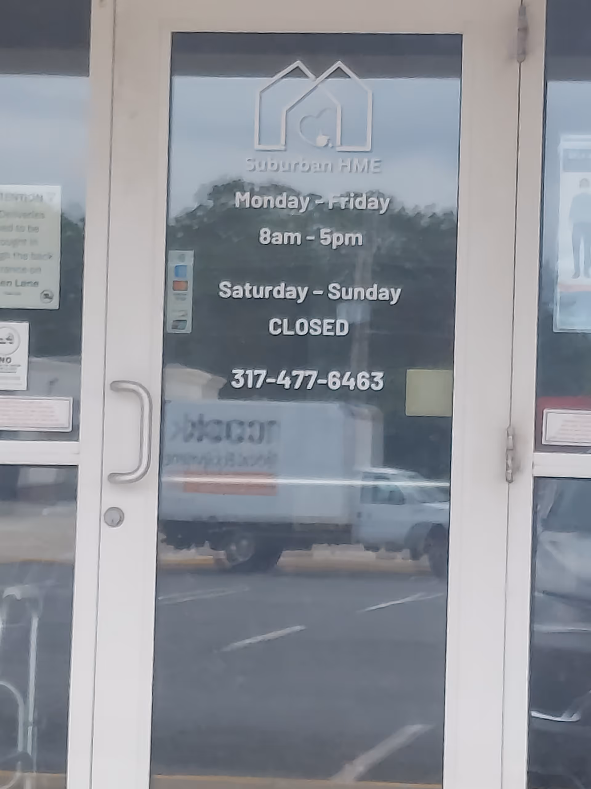 Glass door displaying a logo and business hours, with a reflection of a truck outside.