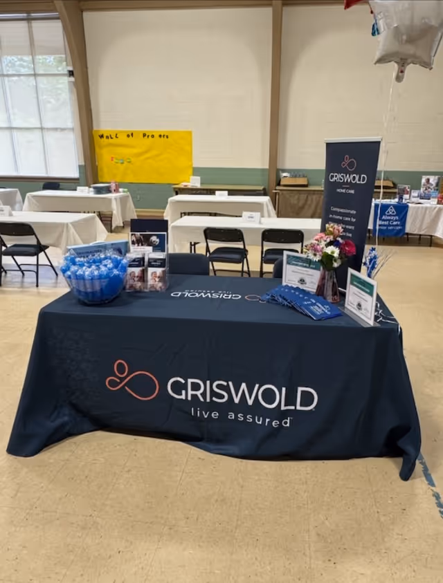 Indoor event booth with Griswold Home Care table, banners, and promotional materials.