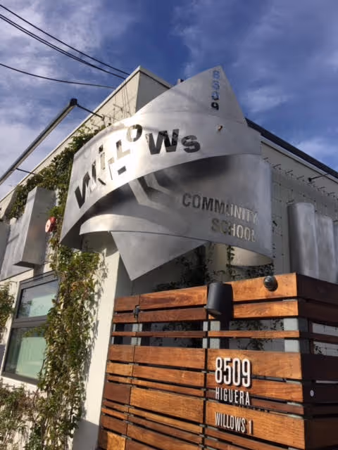 Exterior of Willows Community School with curved metal sign and wooden gate.