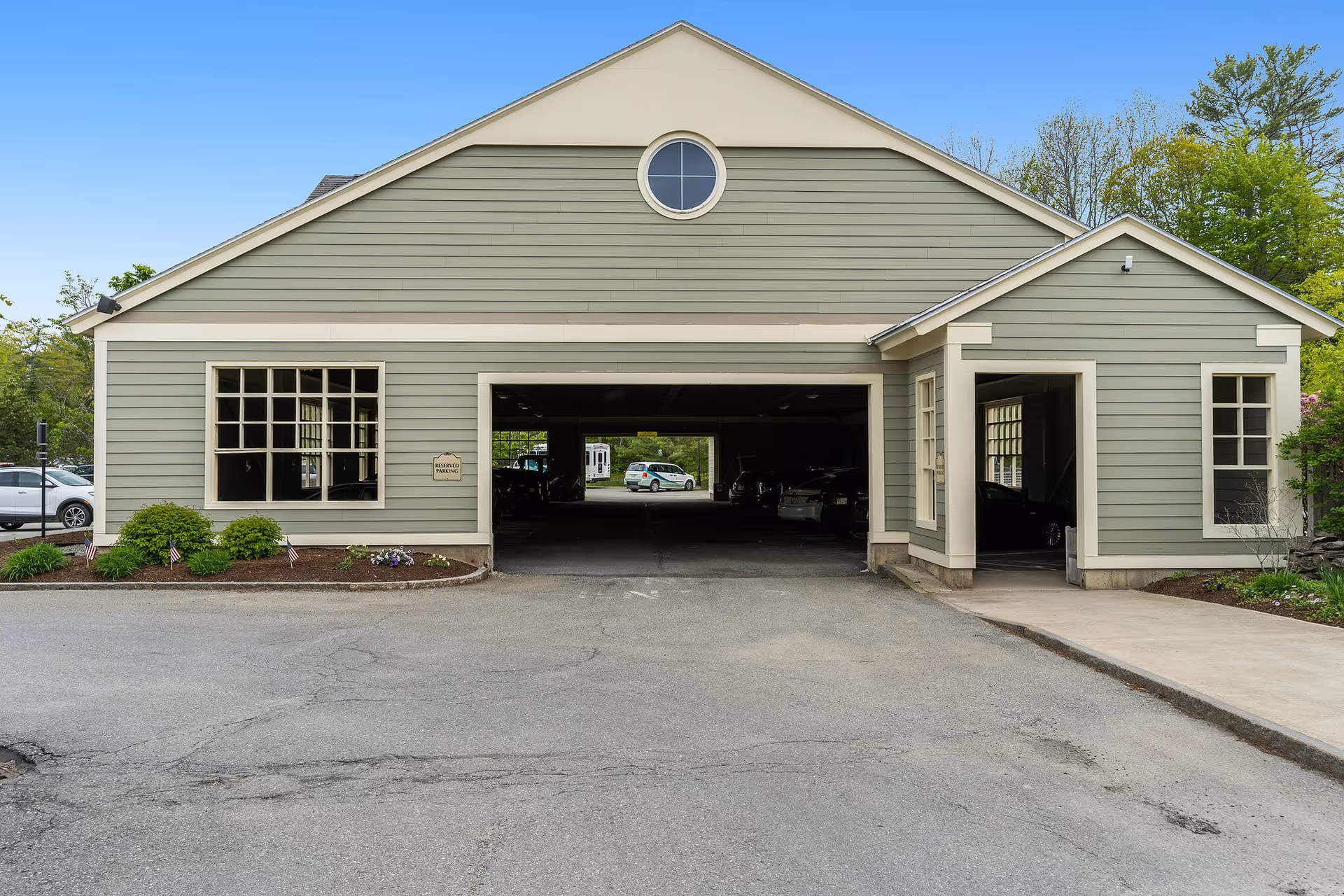 Front exterior of a light green building with a central covered parking/carport, windows, and surrounding landscaping.