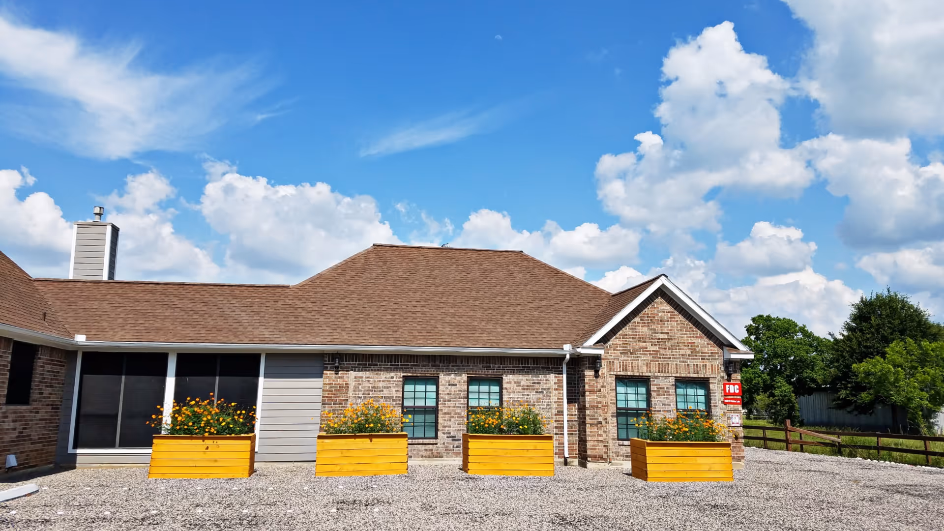 Brick, single-story care facility with yellow planter boxes and a gravel lot.