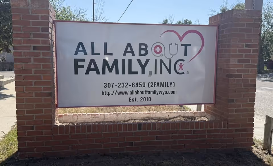 Brick entrance sign reading All About Family, Inc. on a low brick wall.