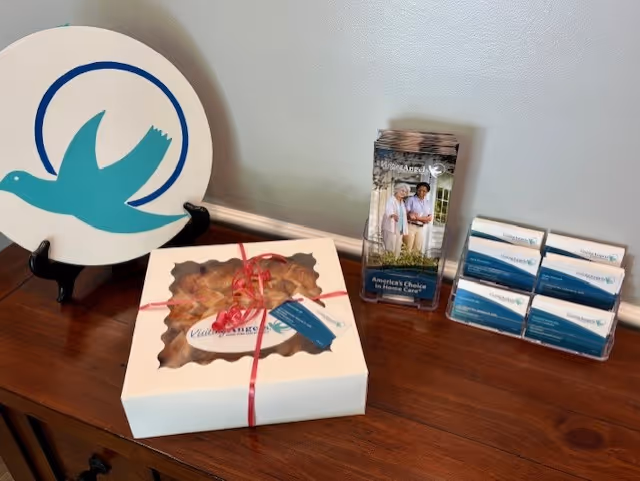 Wooden table displays Visiting Angels promotional materials and logo plate with brochures and a gift box.