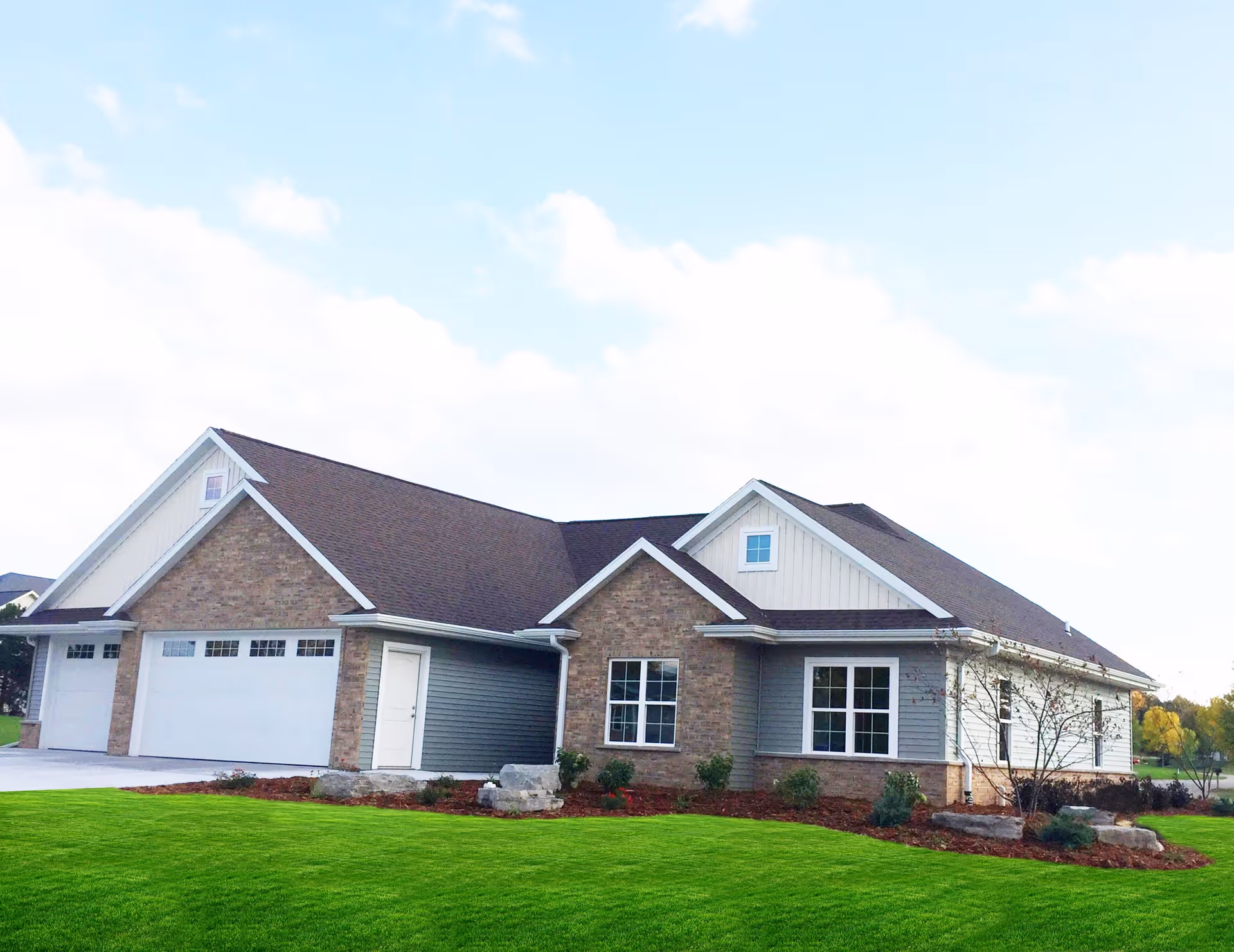 Single-story brick and siding residential-style building with an attached three-car garage and a manicured lawn under a blue sky.